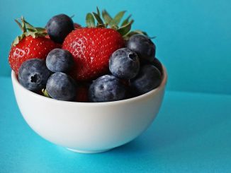 A vibrant mix of fresh strawberries and blueberries in a white bowl on a blue background.