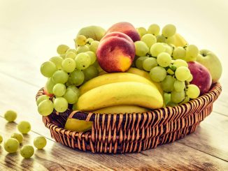 A colorful wicker basket filled with fresh grapes, bananas, and apples on a wooden table.