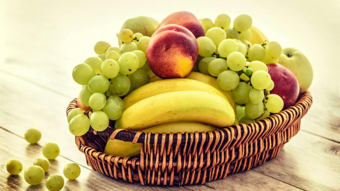 A colorful wicker basket filled with fresh grapes, bananas, and apples on a wooden table.