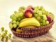 A colorful wicker basket filled with fresh grapes, bananas, and apples on a wooden table.