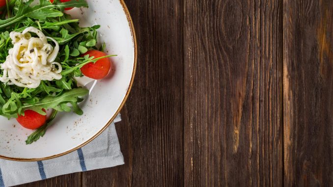 A delightful arugula salad with tomatoes and cheese, served on a rustic wooden table, perfect for healthy eating.