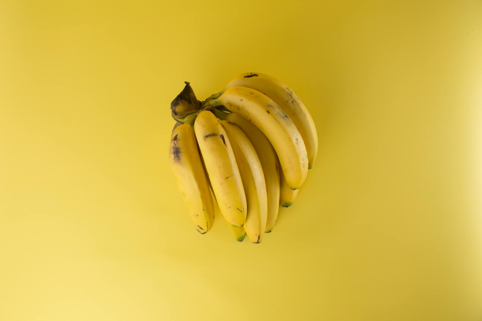 A vibrant bunch of ripe bananas on a matching yellow background, evoking freshness.