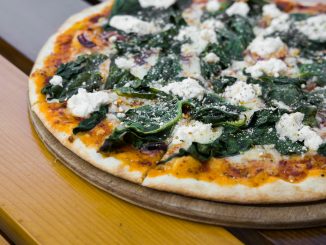 pizza with green leaves on brown wooden table